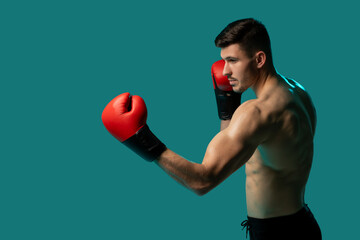A male boxer, wearing red gloves and black shorts, is preparing to throw a punch. He is in a...