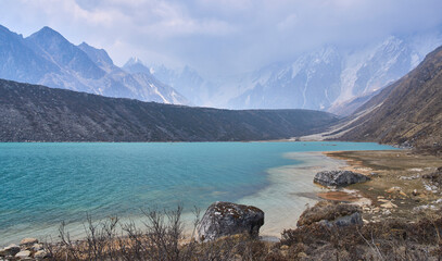 Ponkar lake on descent from Larkya La pass to Bimthang village, Manaslu Circuit.  Foggy and misty spring day in Himalaya. A mountain range in the background. Turquoise color of the lake.