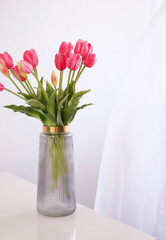 Morning minimalistic bouquet of pink tulips in glass vase on white background. Home comfort concept. Concept for International Women's Day March 8th. Vertical.