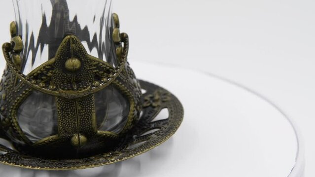 Close-up side view of empty armudu (armuda, bogmaly) - traditional metal and glass tea or coffee cup with small spoon from Turkey or Azerbaijan. Souvenir from travel turning on gray background.