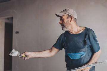 Construction worker wearing worker overall with wall plastering tools renovating apartment house....