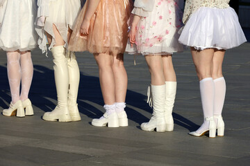 Girls wearing dresses and white socks standing on city street, female legs in white shoes and boots low shoes in a row