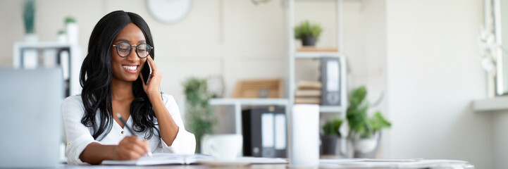 Happy young black woman in formal wear talking on smartphone at workplace, copy space. Beautiful...