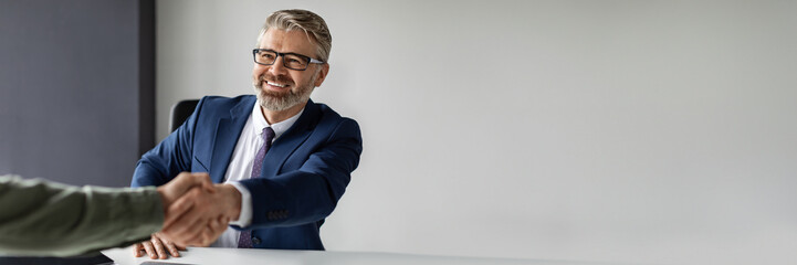 Partnership Concept. Smiling middle aged businessman in suit handshaking with partner in office after signing contract, happy entrepreneur greeting companion after successful deal, copy space