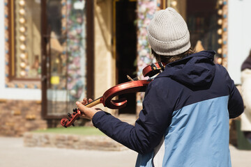 A man on the street is playing the violin, view from the back