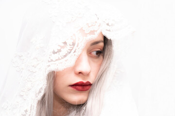 A woman with long gray hair and red lipstick is wearing a white veil