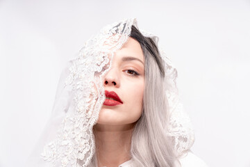 A woman with long gray hair and red lipstick is wearing a white veil