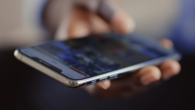 Online life. African guy scrolling social media app on cellphone, close up