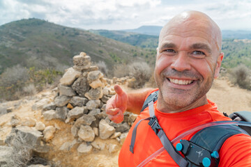 Smiling hiker takes a selfie in the top of a mountain.