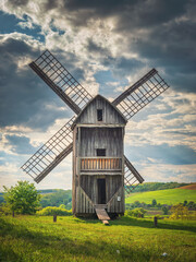 view to back side of old wooden windmill under dramatic sky in spring day