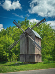 portrait view to old wooden windmill close to road under blue sky with clouds
