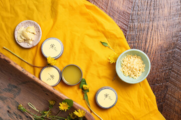 Dandelion salve, shea butter, beeswax, flowers and leaves on wooden table.