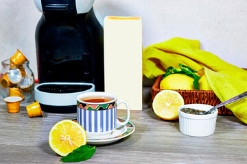 Glass cup with lemon, mint tisane with espresso machine, tea capsule and mockup box on wood table