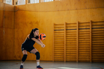 Woman playing volleyball in a sports hall and receiving a ball with a bump