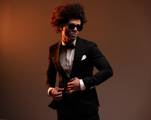 elegant young groom with sunglasses adjusting black tuxedo