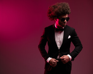 sexy businessman with curly hair looking to side and fixing tuxedo