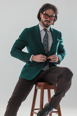 elegant young man with sunglasses buttoning green suit and sitting