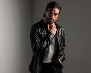 sexy bearded man with glasses in black leather jacket touching neck