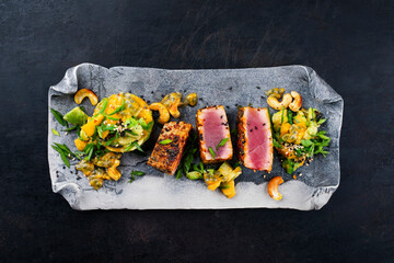 Traditional Japanese gourmet tuna fish steak tataki with tropical fruit tartar and cashew nuts served as top view on a Nordic design tray with copy space