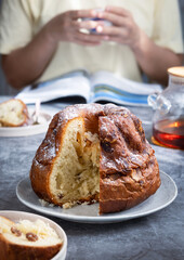 French Klouglof in a plate its sliced piece. While person drink tea in background. It's a cake traditionally baked in a distinctive ring pan, similar to Bundt cake, but leavened with baker's yeast.