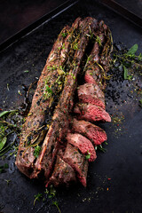 Traditionally roasted saddle of venison with fillet pieces and herbs served as close-up on a rustic metal tray
