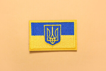 Military badge with trident and flag of Ukraine on beige background
