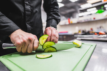 Close-up of hands slicing a cucumber on a green cutting board in kitchen