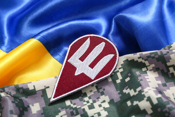Military badge of Ukrainian army with trident and Ukraine flag on camouflaged uniform, closeup