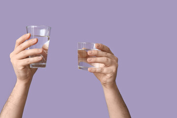 Male hands with glasses of clean water on lilac background