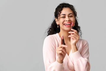 Happy young African-American woman with pink lipsticks on grey background