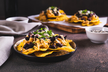 Mexican nacho chips baked with chicken, black beans and cheese on a plate on the table
