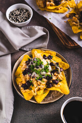 Mexican baked nachos with chicken, black beans and cheese on a plate on the table vertical view