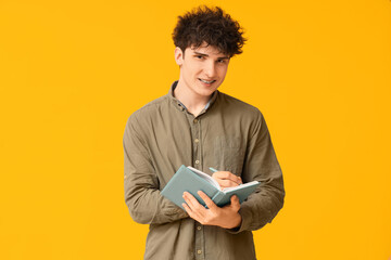 Handsome young businessman with notebook on yellow background