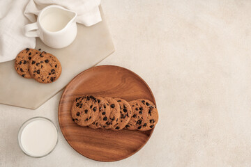 Wooden plate and board of sweet cookies with chocolate chips and glass of milk on white background