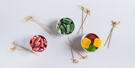 Fruit gummy candies in bowls and skewers for preparing treats top view web banner