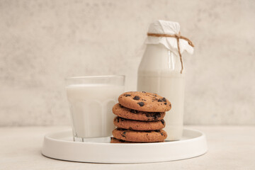 Plate of sweet cookies with chocolate chips and bottle of milk on white background