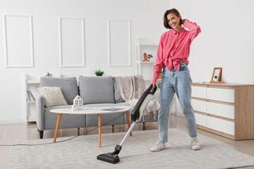 Happy young woman cleaning carpet with handheld vacuum cleaner in living room