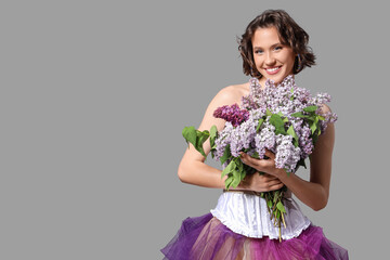 Happy young woman with bouquet of blooming lilac flowers on grey background