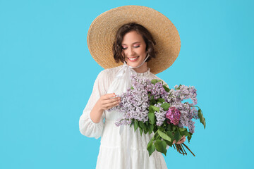 Happy young woman with bouquet of blooming lilac flowers on blue background