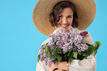 Happy young woman with bouquet of blooming lilac flowers on blue background