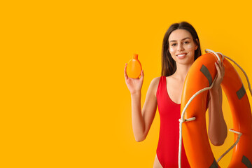 Beautiful young woman with bottle of sunscreen cream and lifebuoy on yellow background
