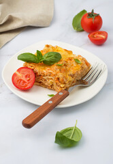 Traditional Italian dish of lasagna with bolognese sauce garnished with basil and tomatoes on a white plate..