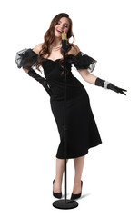Fototapeta premium Beautiful young woman in stylish black dress with microphone singing on white background