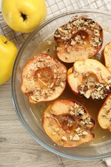 Delicious baked quinces with nuts in bowl and fresh fruits on wooden table, flat lay