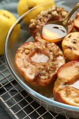 Pouring tasty honey onto baked quinces in bowl on table, closeup