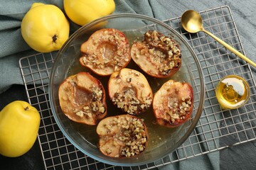 Tasty baked quinces with walnuts and honey in bowl on black table, flat lay