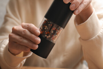Woman grinding pepper with shaker at table, closeup