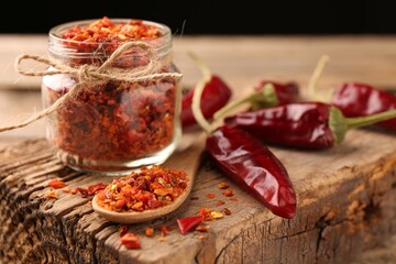 Chili pepper flakes and pods on wooden table, closeup