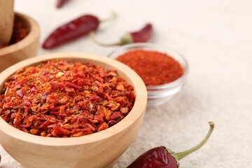 Chili pepper flakes and pods on light textured table, closeup. Space for text