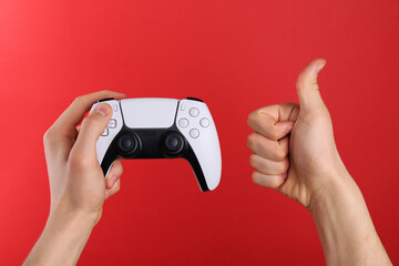 Man using wireless game controller and showing thumbs up on red background, closeup